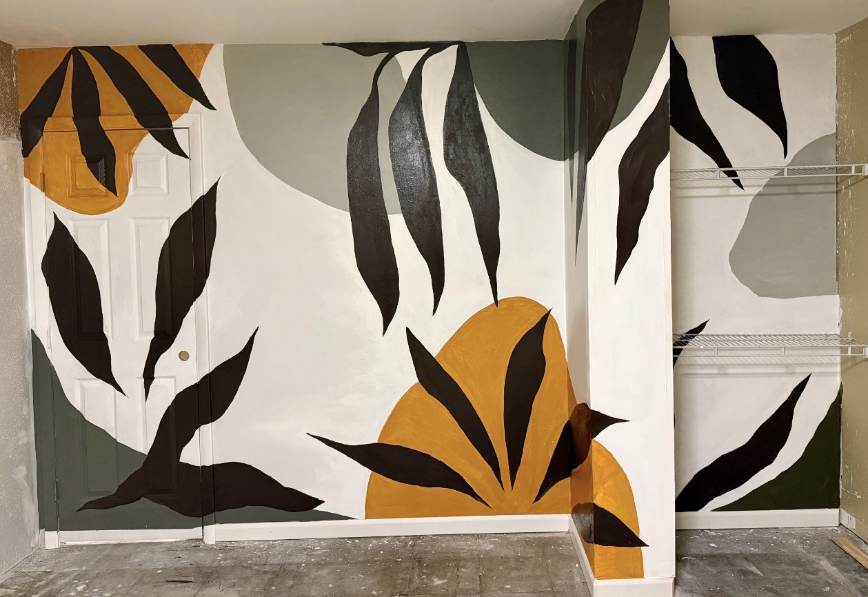 A modern botanical mural with oversized leaves and warm ochre shapes across an interior wall.