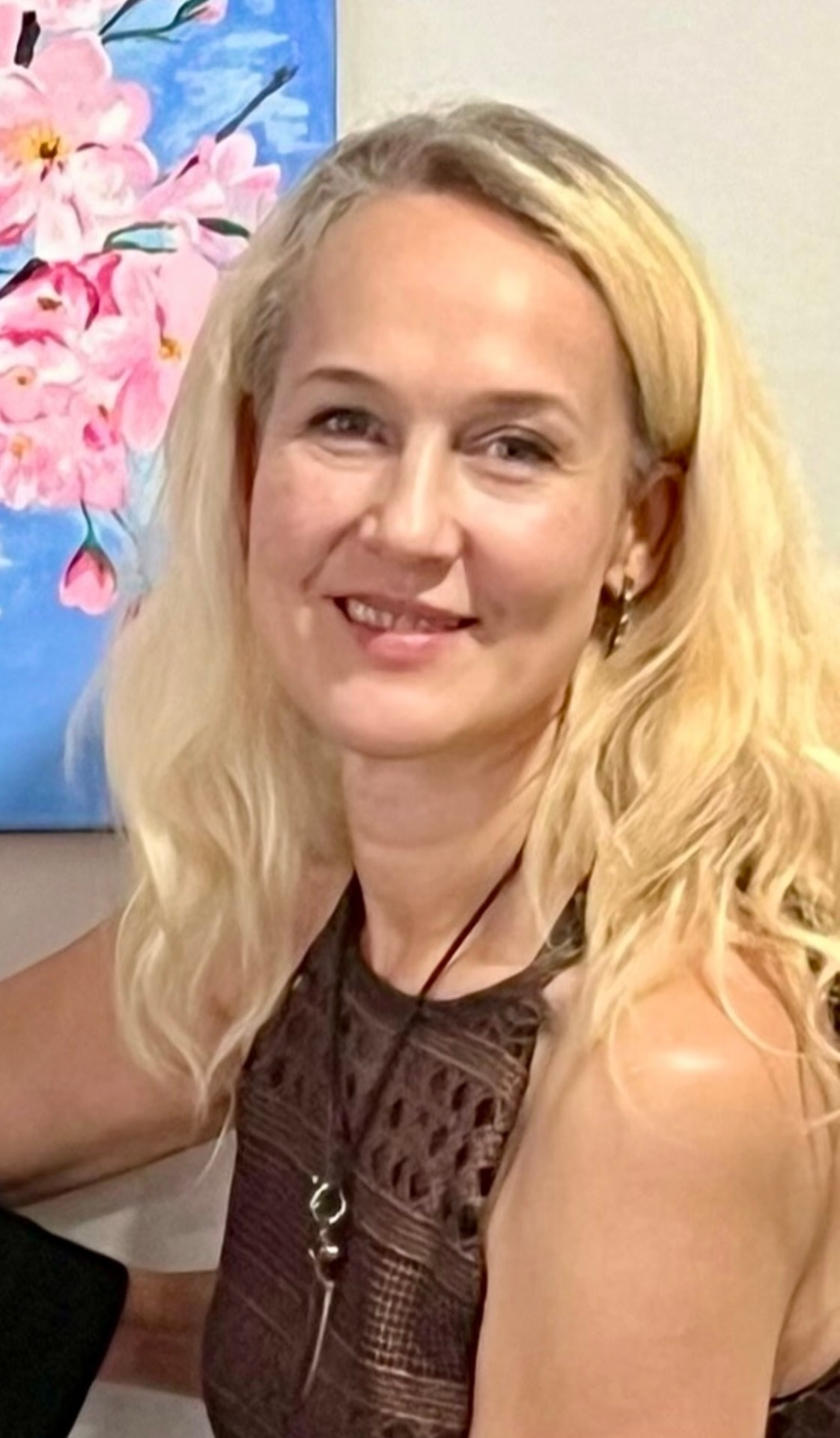 Larisa Harris, custom mural artist in Brevard County, Florida, smiling in front of one of her floral paintings.