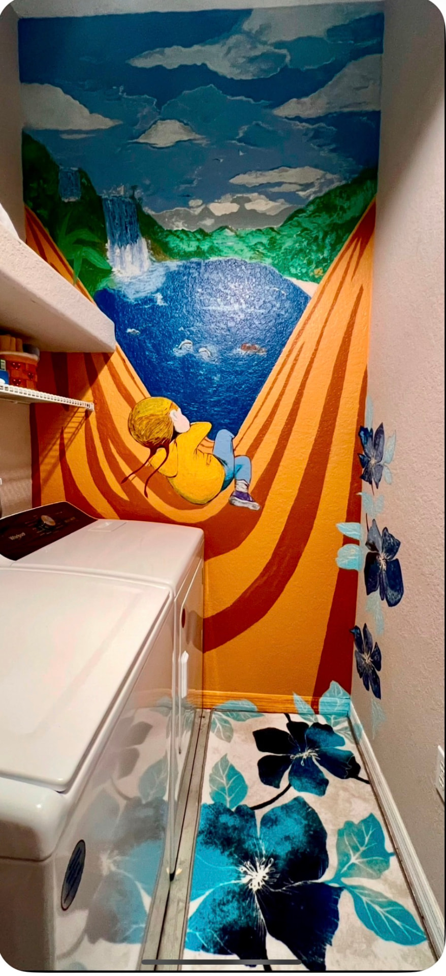 A colorful laundry room mural with a child relaxing in a hammock overlooking a waterfall and mountain lake.