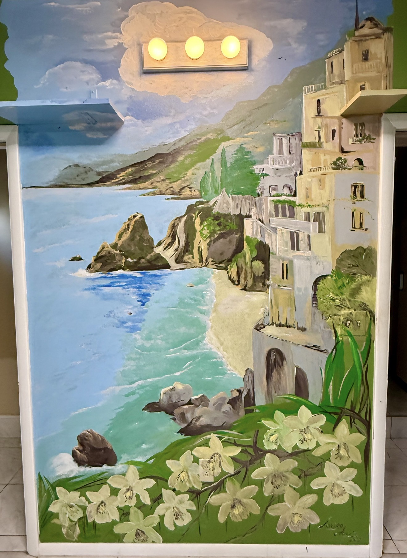 A hand-painted coastal village mural with cliffs, blue water, flowers, and seaside buildings.
