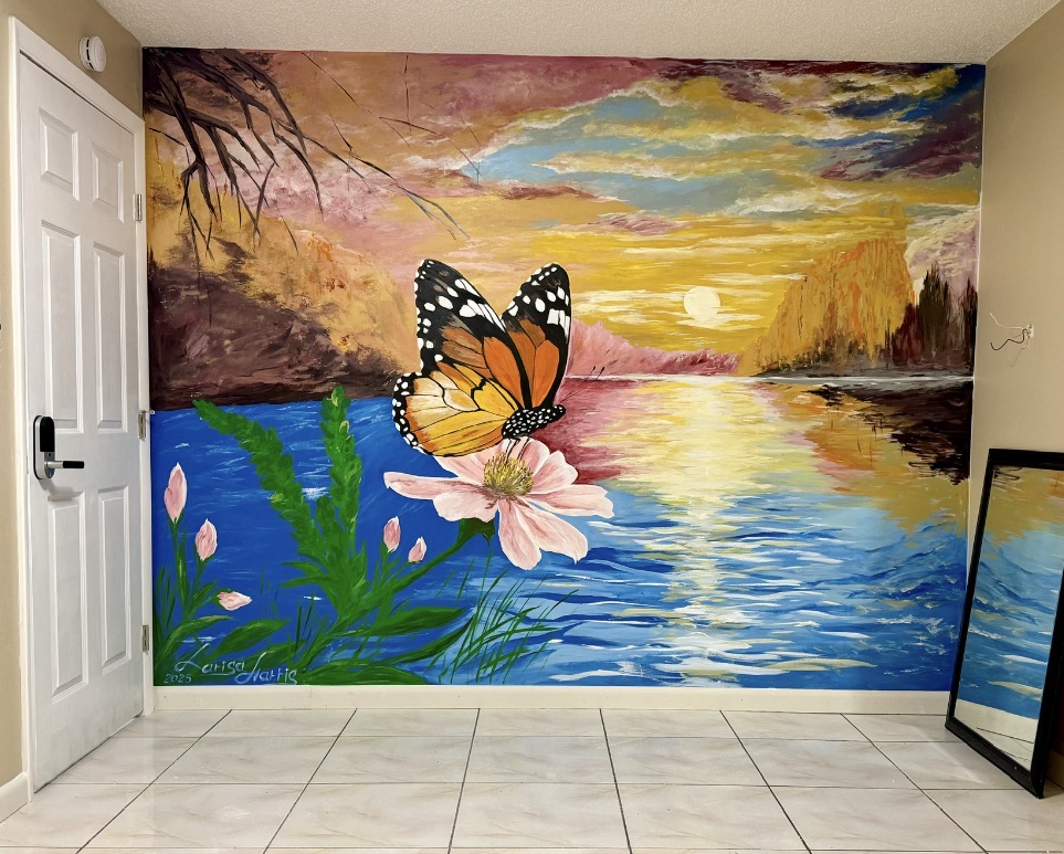 A wall mural of a monarch butterfly over a pink flower beside a sunset lake.