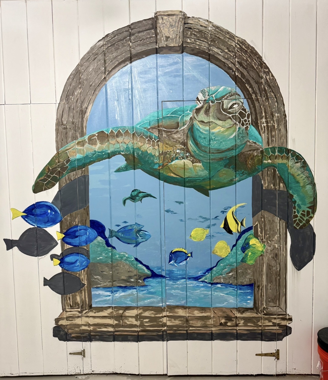 A sea turtle and tropical fish mural painted around a faux window on paneled doors.